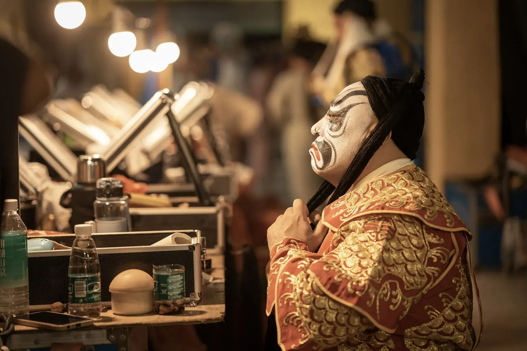 An opera performer applying makeup at a mirror backstage