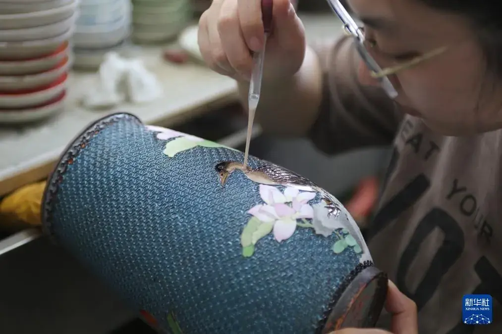Enamel being applied to the curved blue body of a vessel