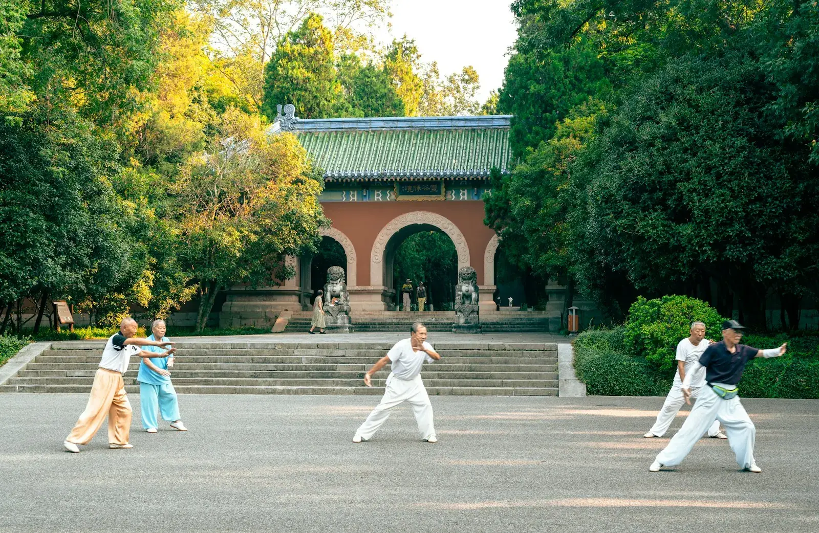 People practising tai chi in a courtyard before a traditional gate