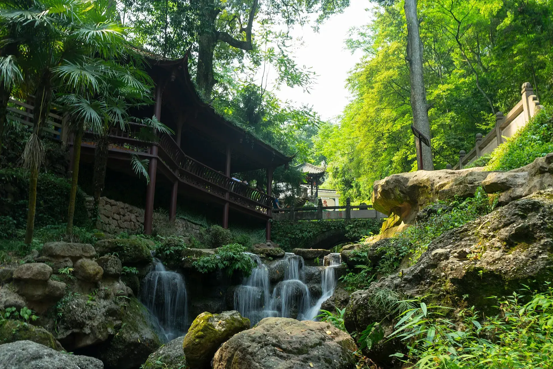 A covered wooden walkway above a mossy cascade on the mountain