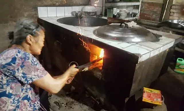 An elderly woman firing tea over a wood-fired stove