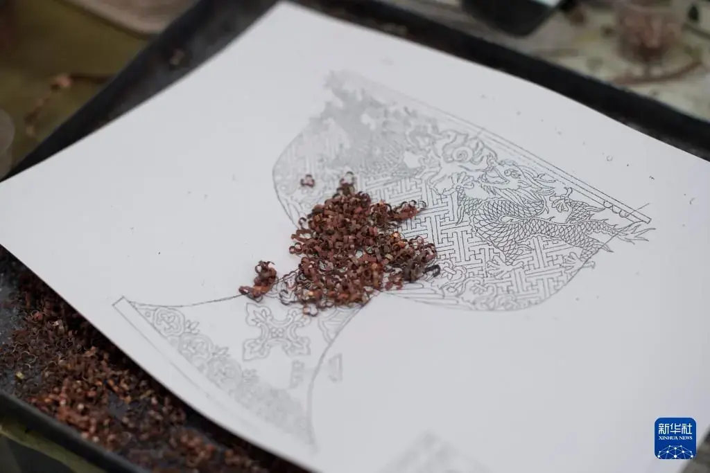 Fine copper wire being laid onto a white design to form a cloisonné pattern