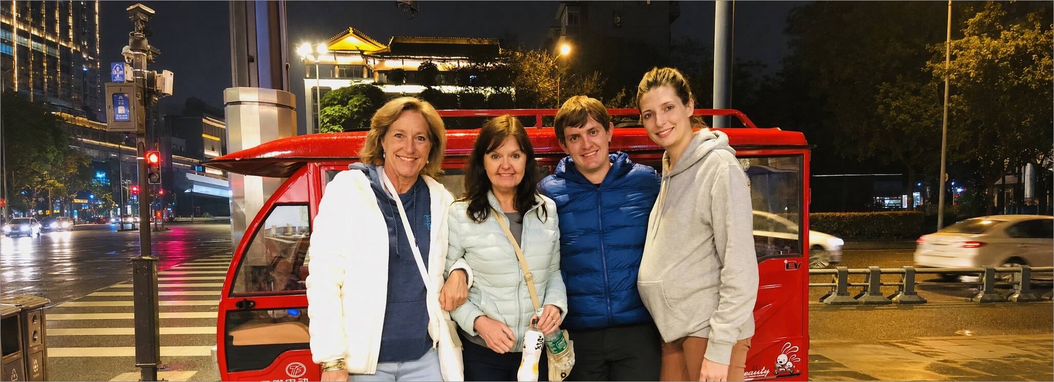 Four travelers posing with their red tuk-tuk on a Chengdu street