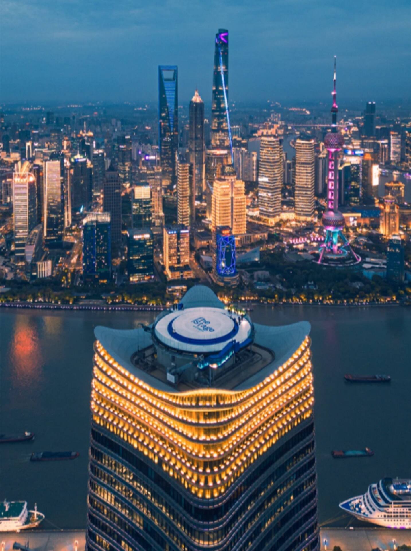 The lit Magnolia Plaza on the river, a round helipad on the roof, Lujiazui beyond