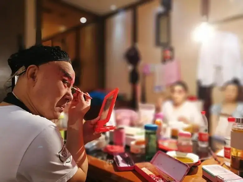 A Sichuan opera performer applying face paint at a mirror