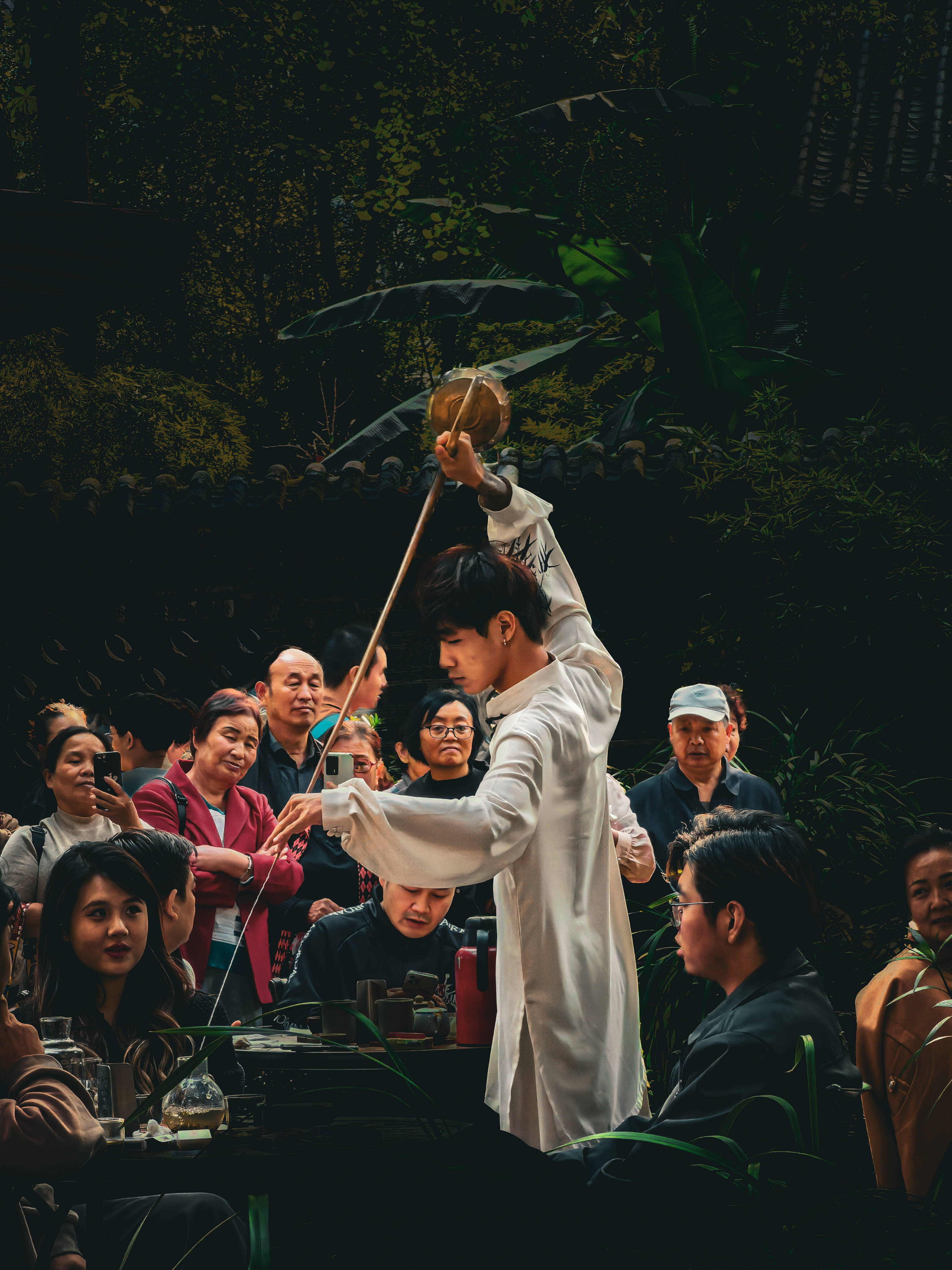 Visitors holding gaiwan tea at a shaded outdoor teahouse table