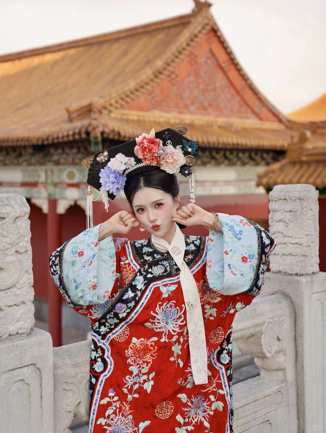 A visitor in Qing court dress and banner headdress in front of a red wall