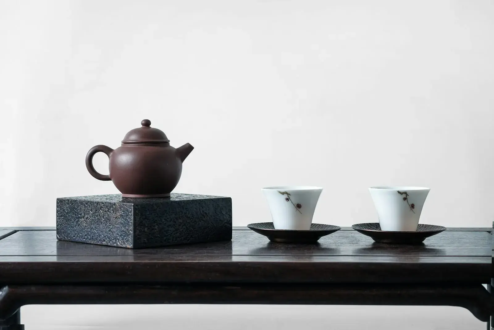 A purple-clay teapot and two white cups on a dark tea table