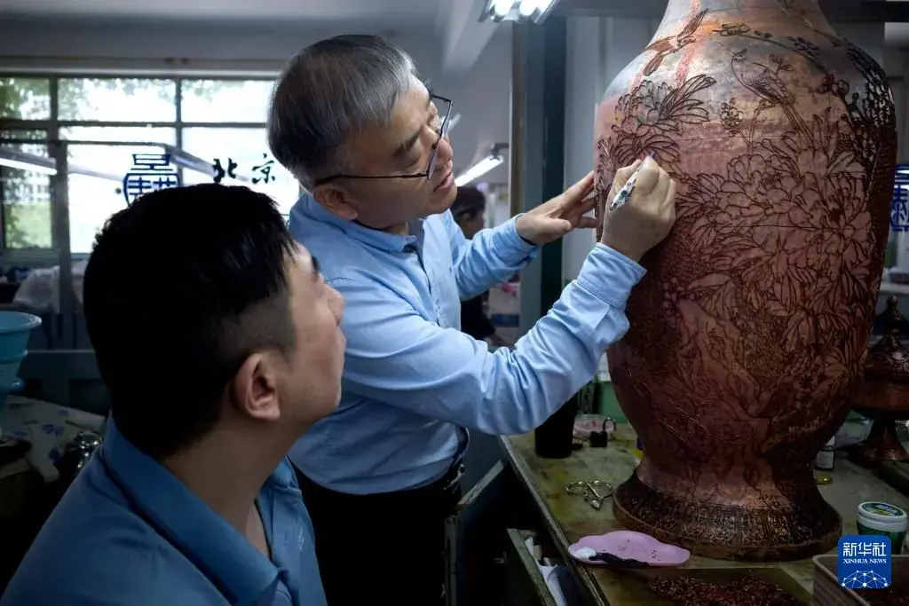 Two craftsmen working on a large cloisonné piece
