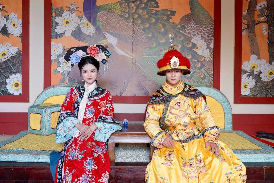 An emperor in a dragon robe and an elaborately dressed empress seated side by side on the throne