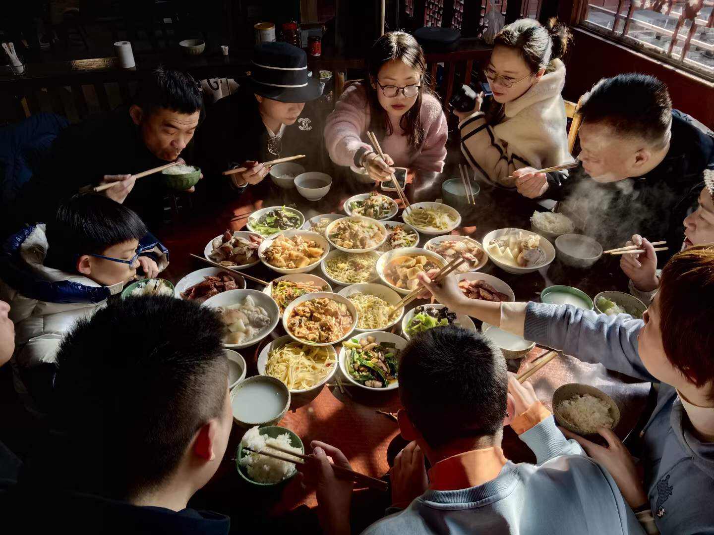 Guests and a Taoist sharing a steaming table of mountain dishes in the temple canteen