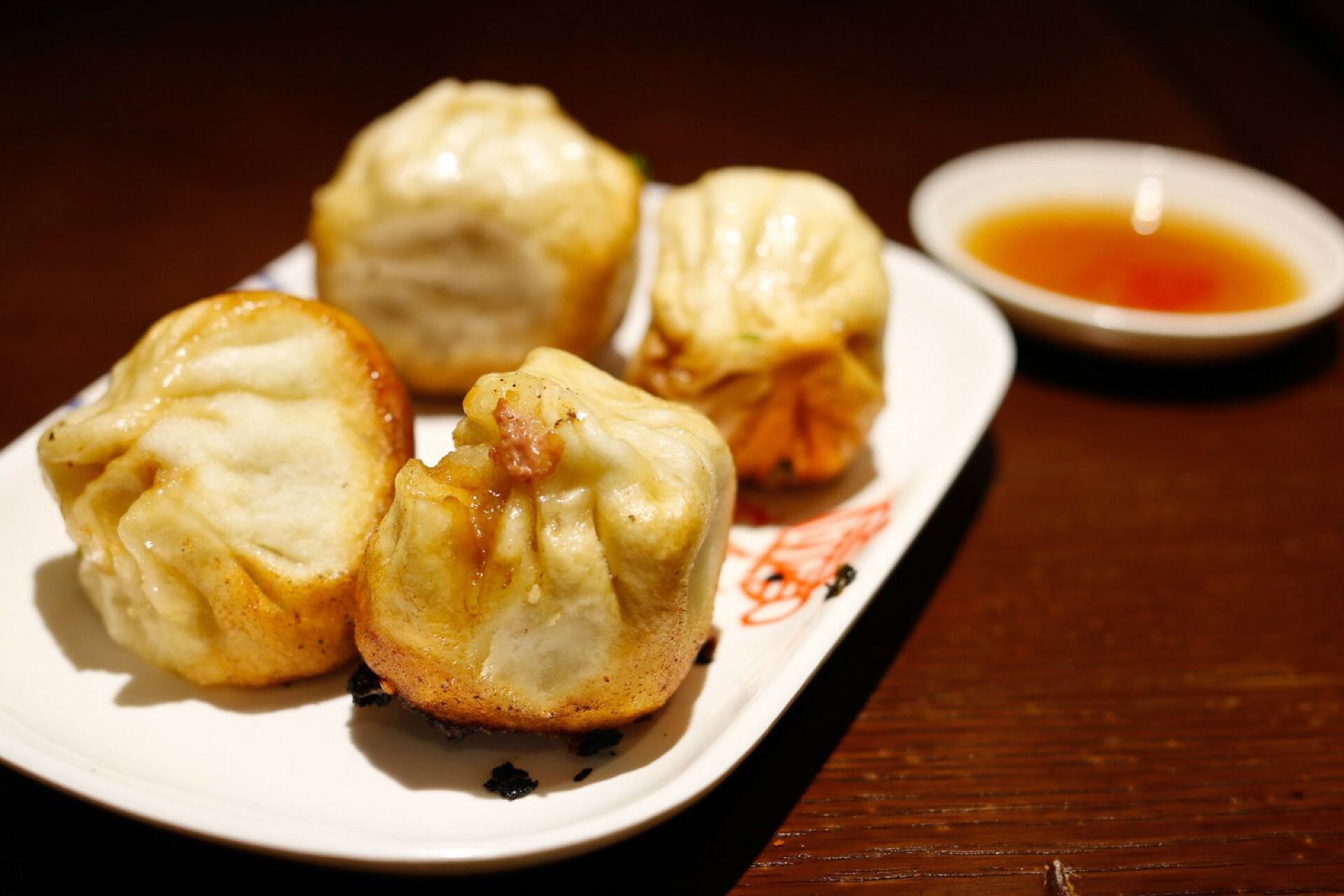 Pan-fried buns on a plate, with a bowl of dipping sauce
