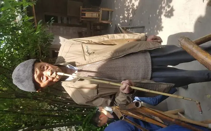 An elderly man in a conical hat carrying a shoulder pole through the town